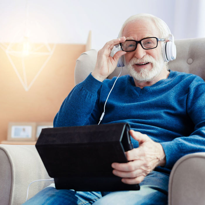 Elderly man sitting in a chair watching a tablet with headphones on