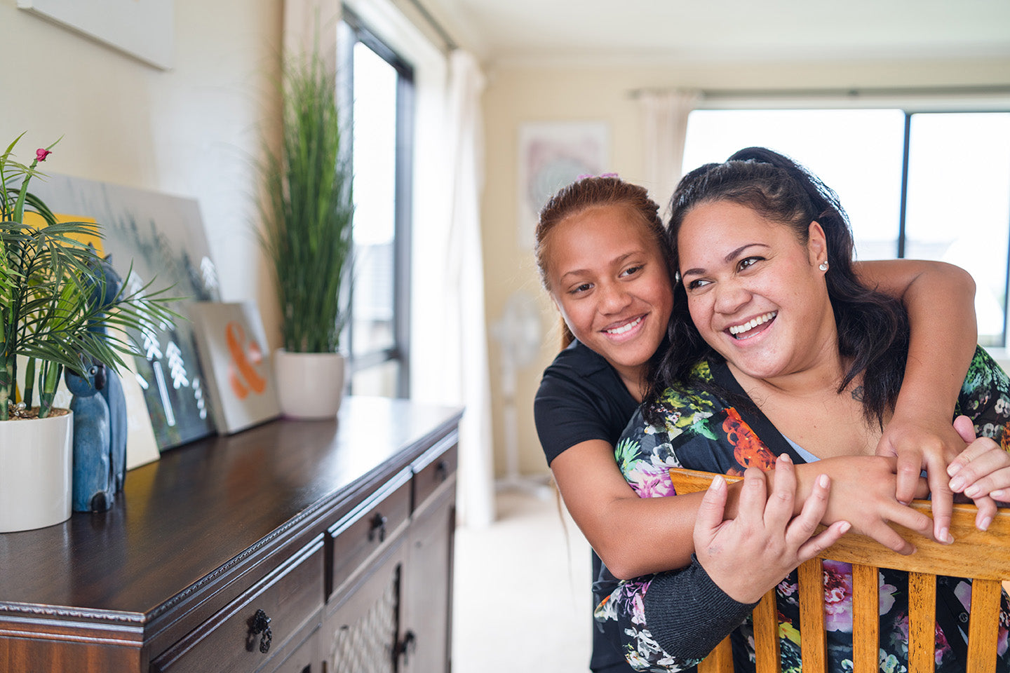 Two young female family members smiling and hugging each other in their home