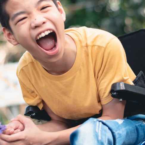 Young child in a wheelchair smiling in a yellow tshirt
