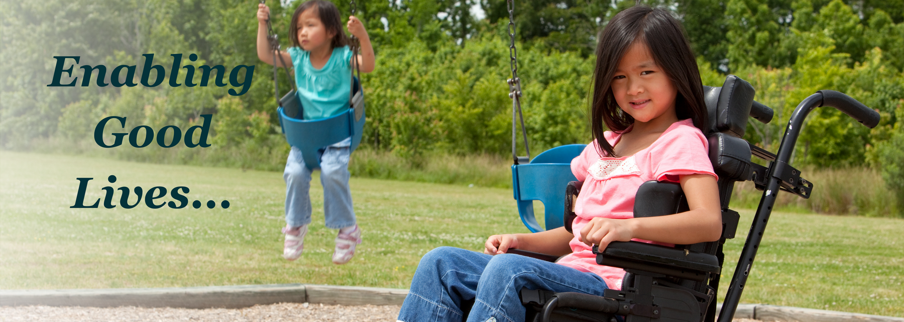 Two children at a playground, one in a wheelchair and one on a swing