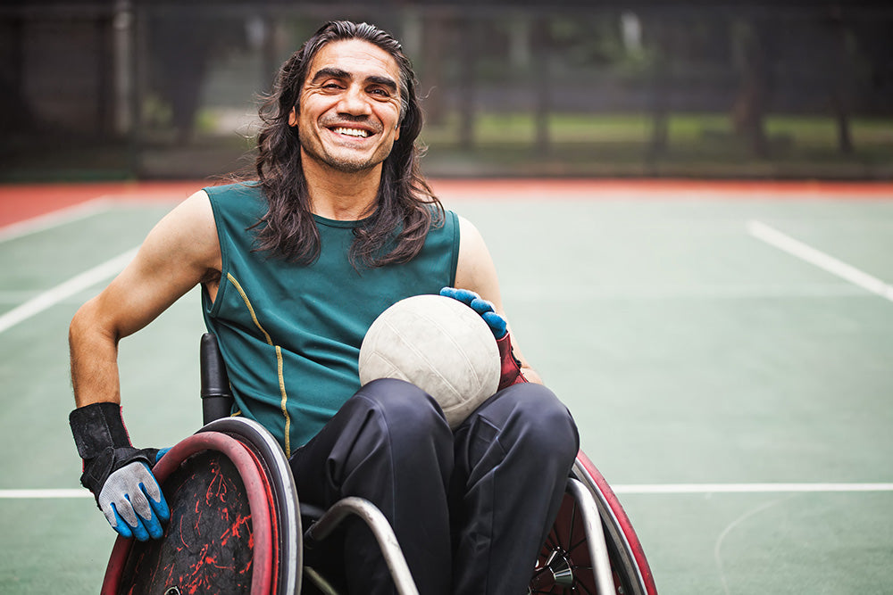 A smiling man in a wheelchair on a basketball court dressed in exercise gear
